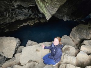 Vrouw bij een diepblauw waterbassin in een lavagrot in het vulkanische landschap van IJsland