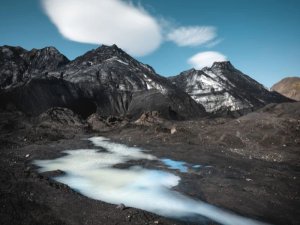 Dunkle vulkanische Berge und ein milchiger Fluss im rauen Hochland Islands unter klarem Himmel