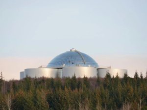Glasüberdachtes Gebäude mit silbernem zylinderförmigem Sockel ragt über einem dichten Wald in Island