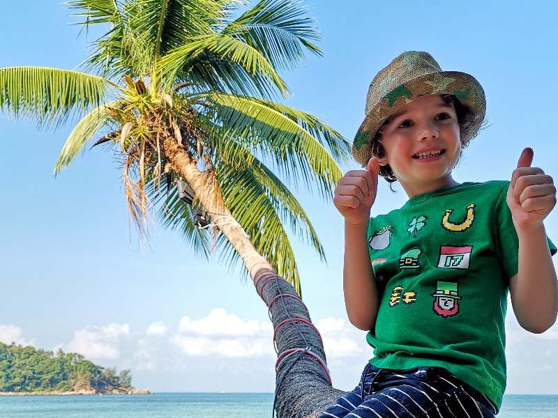 Kind sitzt auf Palme am Strand in Thailand