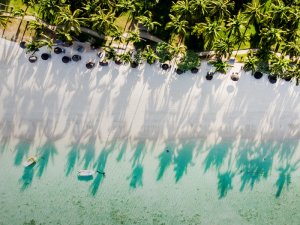 Luftaufnahme eines tropischen Strandes mit Palmen, die lange Schatten auf weißen Sand und türkisfarbenes Wasser mit zwei Booten werfen in Südafrika