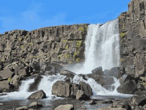 Waterval tussen donkere basaltrotsen in het ruige landschap van IJsland onder een heldere blauwe lucht