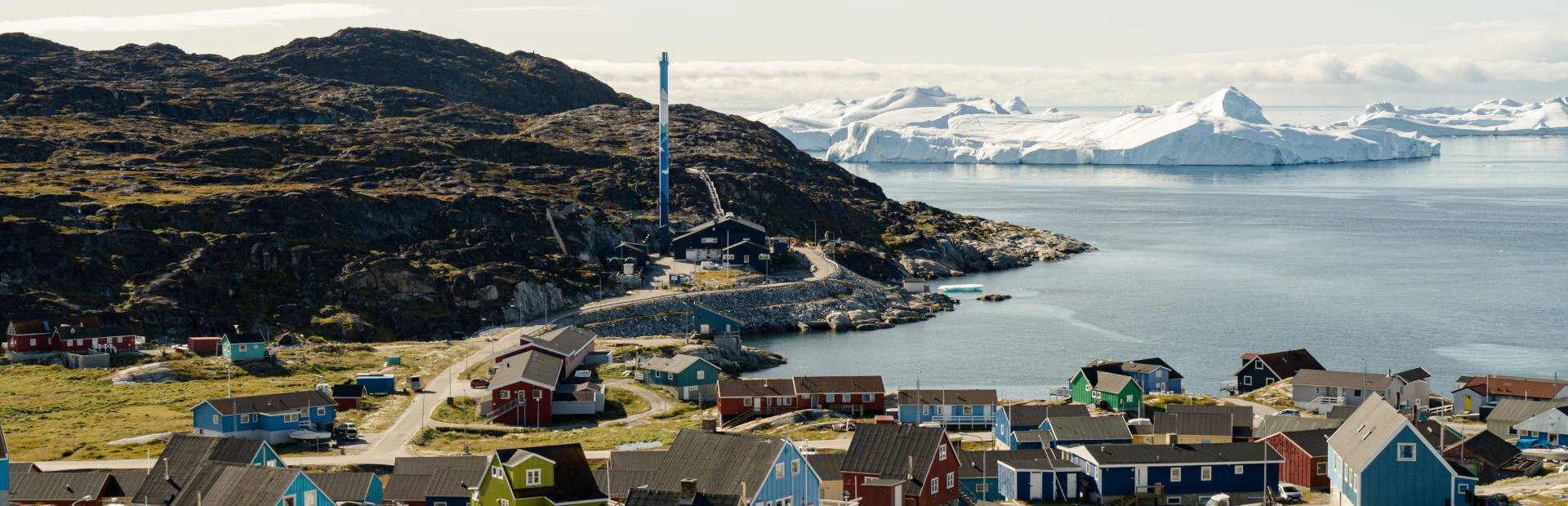 Farbenfrohes Dorf an einem Fjord mit Eisbergen und felsigen Hügeln an der Küste von Grönland