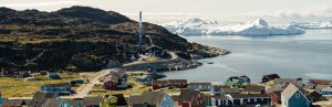 Farbenfrohes Dorf an einem Fjord mit Eisbergen und felsigen Hügeln an der Küste von Grönland
