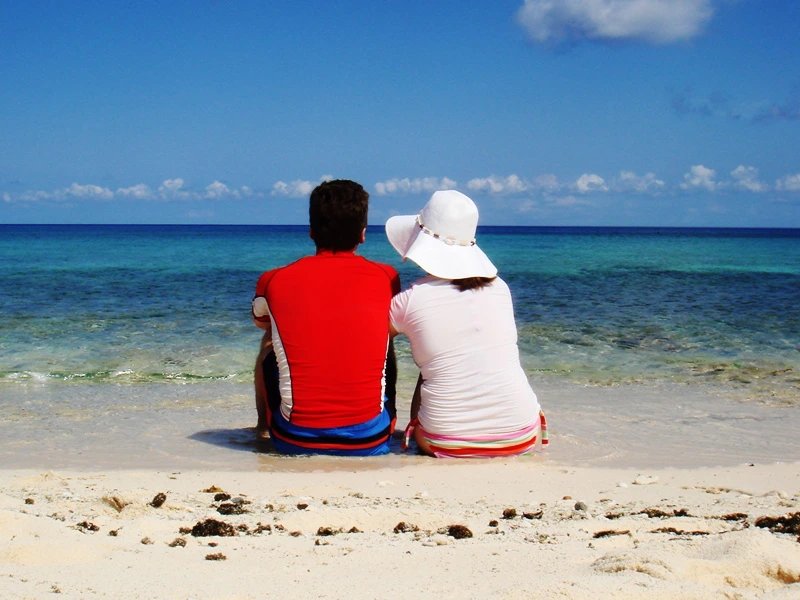 Zwei Menschen sitzen am Sandstrand und blicken auf den Ozean in Tulum, Mexiko