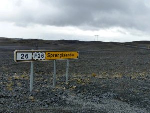Gelb-weißes Straßenschild für die Routen 26 und F26 Richtung Sprengisandur in einer weiten felsigen Landschaft unter bewölktem Himmel in Island