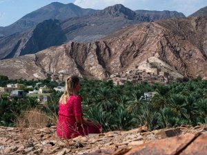 Reisende auf einem Fels mit Aussicht auf die Berge von Misfat Al Abriyeen, Oman