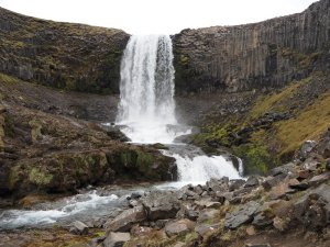 Mächtiger Wasserfall stürzt über eine Klippe mit markanten sechseckigen Basaltsäulen auf der rechten Seite in Island