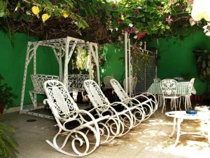 Außenpatio mit leuchtend grüner Wand, weißen schmiedeeisernen Schaukelstühlen, Schaukel und Esstisch unter einem grünen Blätterdach in Baracoa, Kuba