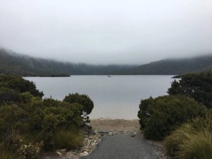 See in Australien umgeben von nebelverhangenen Bergen mit einem kleinen Boot auf dem Wasser und grünen Sträuchern im Vordergrund