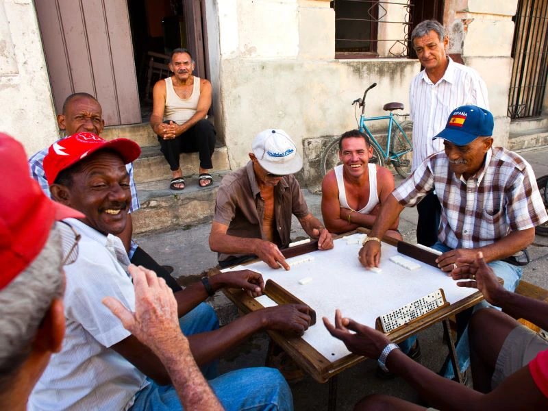 Gruppe lächelnder Männer unterschiedlichen Alters spielt Domino im Freien in Havanna, Kuba