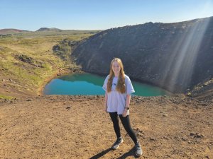 Frau an einem türkisblauen Kratersee in der vulkanischen Landschaft Islands bei sonnigem Wetter