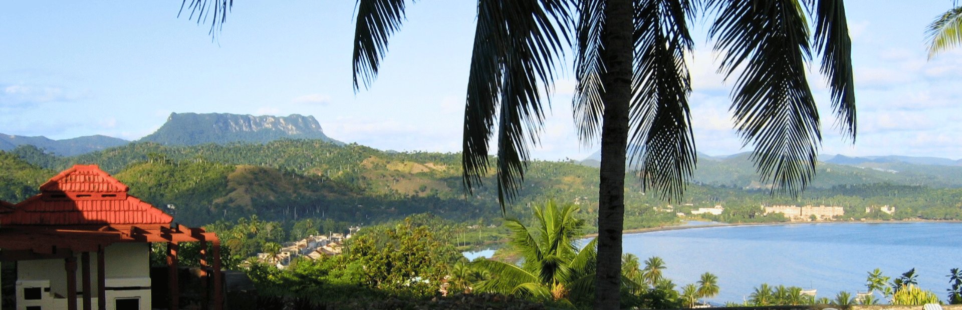 Panoramische tropische Landschaft mit rotem Dach, grünen Hügeln, Tafelberg und Bucht zwischen Palmen in Baracoa, Kuba