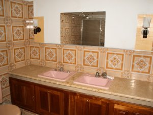 Badezimmer mit gemusterten orangefarbenen Wandfliesen, zwei rosa Waschbecken, Holzwaschtisch und Spiegel in Baracoa, Kuba