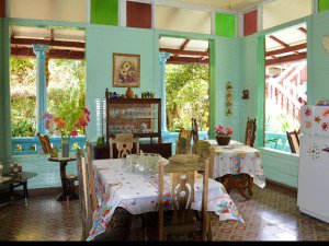 Farbenfrohes Esszimmer mit hellgrünen Wänden, gemustertem Boden, Esstischen und großen Fenstern mit Blick auf einen tropischen Garten in Baracoa, Kuba