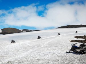 Schneemobile fahren über eine weite Schneelandschaft in den Bergen Islands unter klarem Himmel