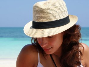 Lächelnde Frau mit Strohhut blickt am Strand auf das Meer in Tulum, Mexiko