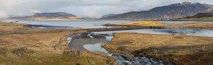 Panoramische Landschaft eines Fjords in Island mit Fluss, Dammstraße, Bergen in der Ferne und einem kleinen Dorf