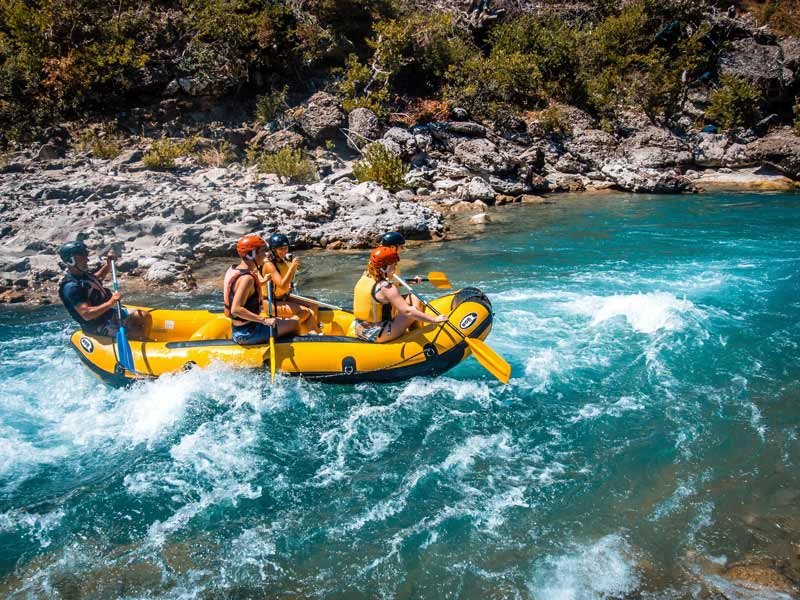 Vier Personen im gelben Raft fahren durch Stromschnellen auf blaugrünem Fluss, Albanien