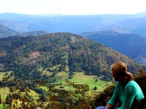 Frau im türkisfarbenen Oberteil mit Blick auf eine weite Berglandschaft mit Wäldern und grünen Tälern in Bled Slowenien