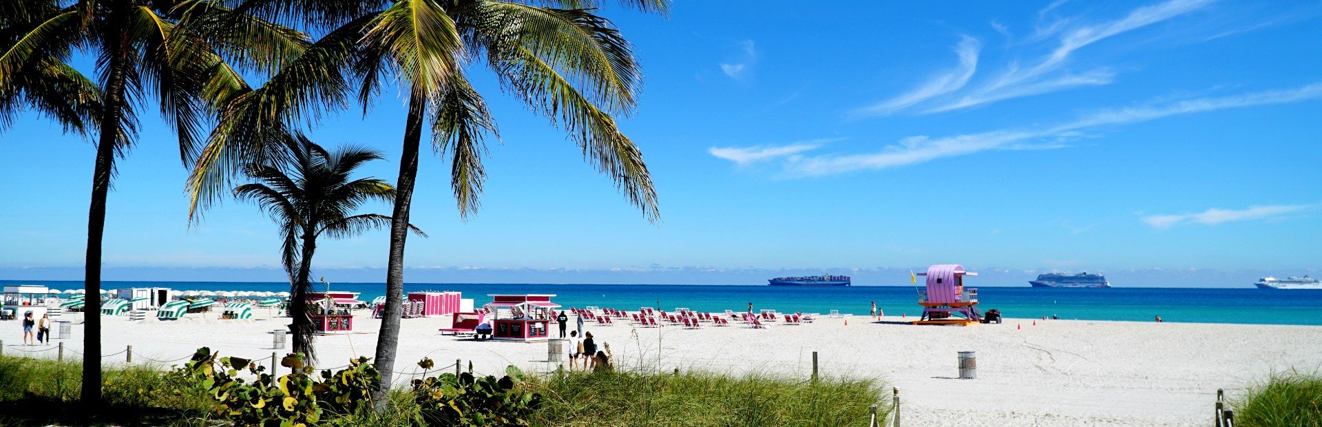 Strandliegen am palmengesäumten Strand mit großen Schiffen im Hintergrund im Wasser