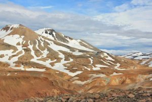 Rotbraune Berge mit Schneefeldern unter einem teilweise bewölkten Himmel in Island
