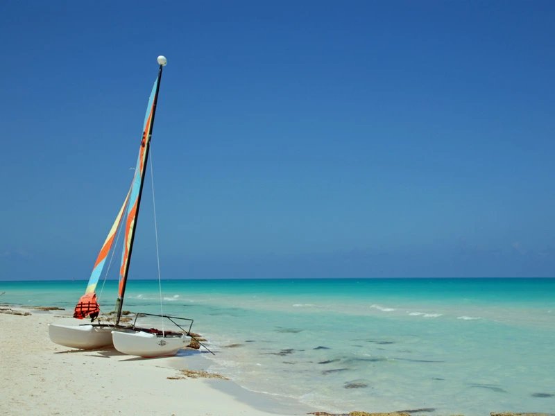 Bunter Katamaran am Sandstrand neben türkisfarbenem Meer unter klarem blauem Himmel in Cayo Santa María, Kuba
