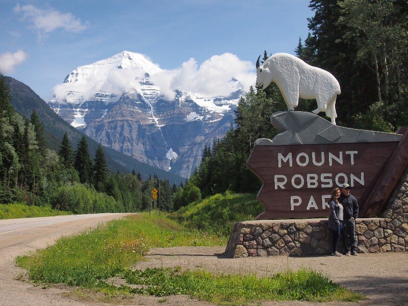Paar vorm Eingangsschild des Mount Robson Parks, im Hintergrund schneebedeckte Berge, Kanada Jasper