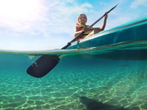 Geteilte Aufnahme eines Kajakfahrers im klaren Wasser in Australien mit Paddel über Wasser und sandigem Meeresboden unter Wasser