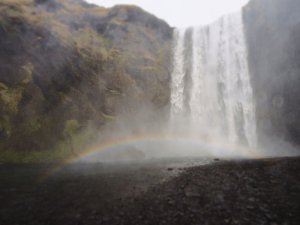 Großer Wasserfall mit einem leuchtenden Regenbogen im Sprühnebel am Fuß des Wasserfalls in Island