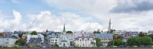 Panoramablick auf Reykjavík am Wasser mit bunten Gebäuden, einer Kirche mit grünem Turm und der Hallgrímskirkja unter bewölktem Himmel in Island