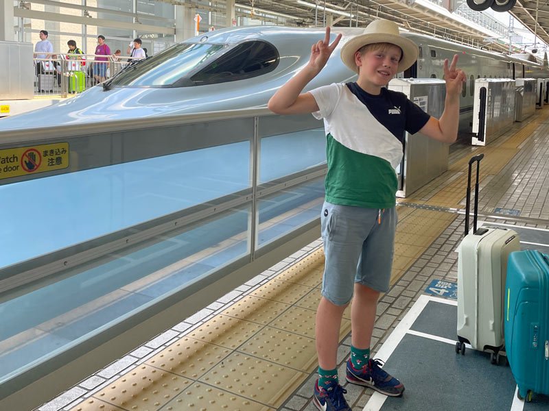 Junge am Bahnsteig in Tokio, während ein Shinkansen einfährt.