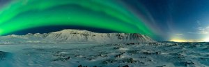 Panoramablick auf grünes Nordlicht über schneebedeckten Bergen und felsiger Landschaft unter einem Sternenhimmel in Island