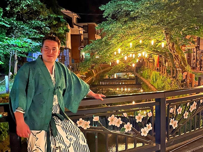 Reisender auf einer Brücke in Kinosaki Onsen bei Nachtbeleuchtung in Japan