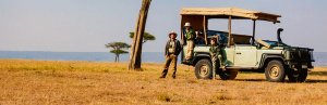 Familie auf Safari neben einem offenen Geländewagen in der Savanne von Südafrika mit weiter Graslandschaft und vereinzelten Bäumen