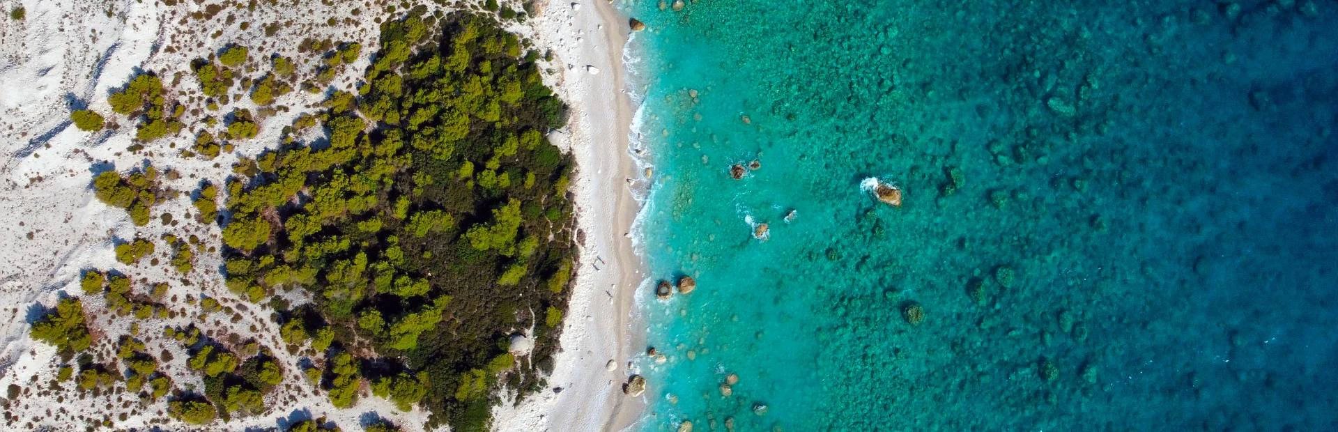 Luftaufnahme weißer Strand in Albanien zwischen grünen Bäumen und türkisfarbenem Wasser