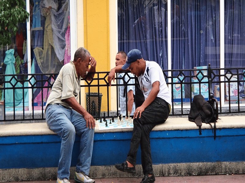 Zwei Männer spielen Schach auf einer Bank, während ein dritter Mann zuschaut in Havanna, Kuba