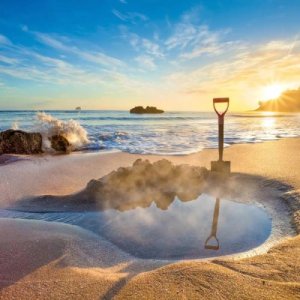 Ein dampfendes Wasserloch vor dem Ozean bei Sonnenuntergang, Coromandel, Neuseeland