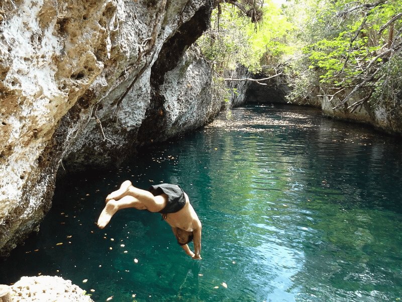Person springt kopfüber in ein klares blaugrünes Naturbecken, umgeben von Felsen und tropischem Dschungel in Semuc Champey, Guatemala