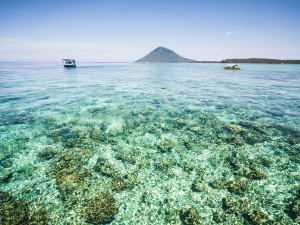 Auf dem Korallenriff in Bunaken im flachen Wasser mit Booten und Vulkan am Horizont in Sulawesi in Indonesien