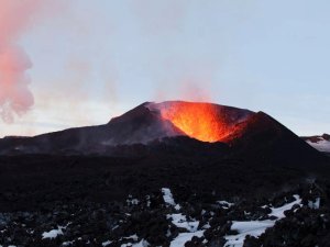 Aktiver Vulkan mit glühender Lava und schwarzen Lavafeldern in der rauen Landschaft Islands