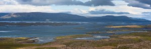 Panoramablick auf eine Bucht mit zahlreichen kleinen grünen Inseln und Bergen in der Ferne unter bewölktem Himmel in Island
