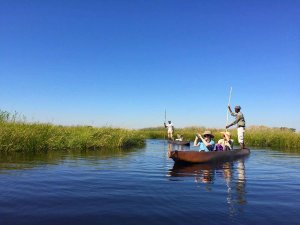 Mokoros mit Touristen und Guides auf einem schilfbewachsenen Fluss unter klarem blauem Himmel in Botswana