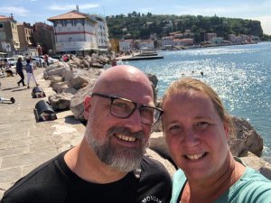 Lächelnder Mann und Frau machen ein Selfie mit Blick auf die Küstenstadt Piran und das glitzernde Meer im Hintergrund in Piran Slowenien