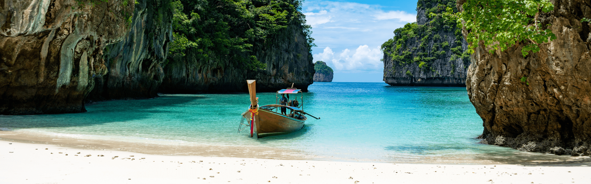 Longtailboot liegt am Strand einer Bucht mit Karstfelsen in Südthailand