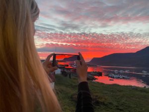Person filmt einen spektakulären roten Sonnenuntergang über einer Bucht mit Bergen und Booten in Grönland