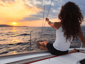 Frau schaut von einer Segelyacht aus dem Sonnenuntergang zu in Sardinien