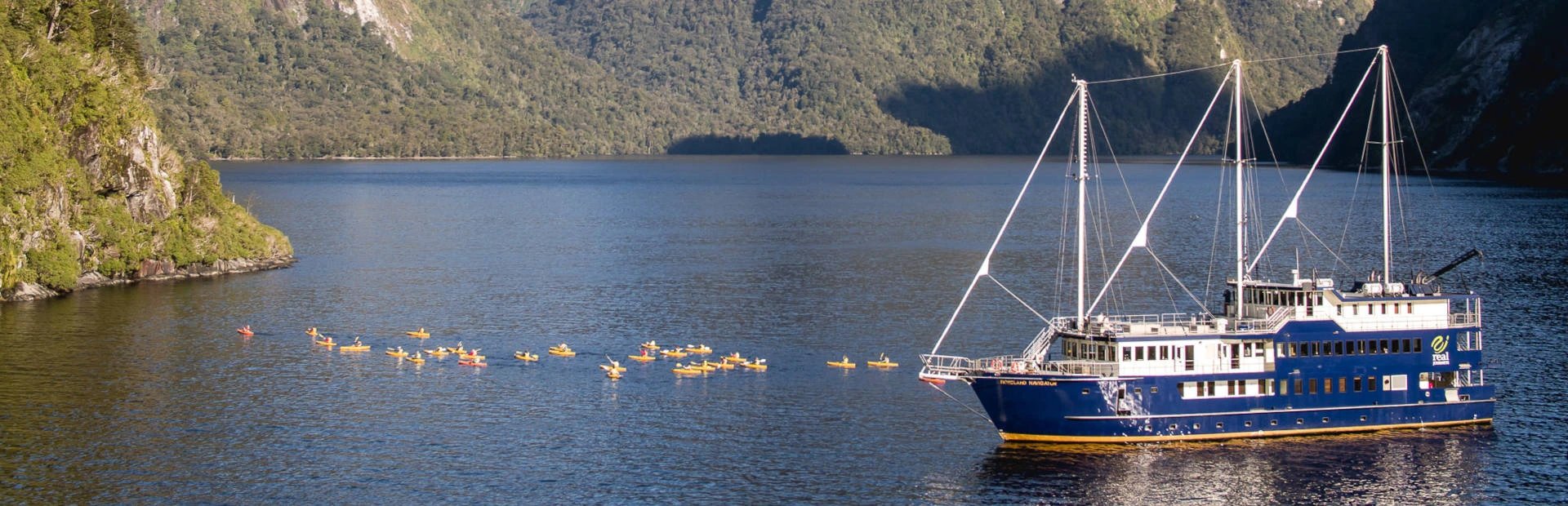 Gruppe von Kajakfahrern neben einem großen Schiff im Doubtful Sound in Neuseeland