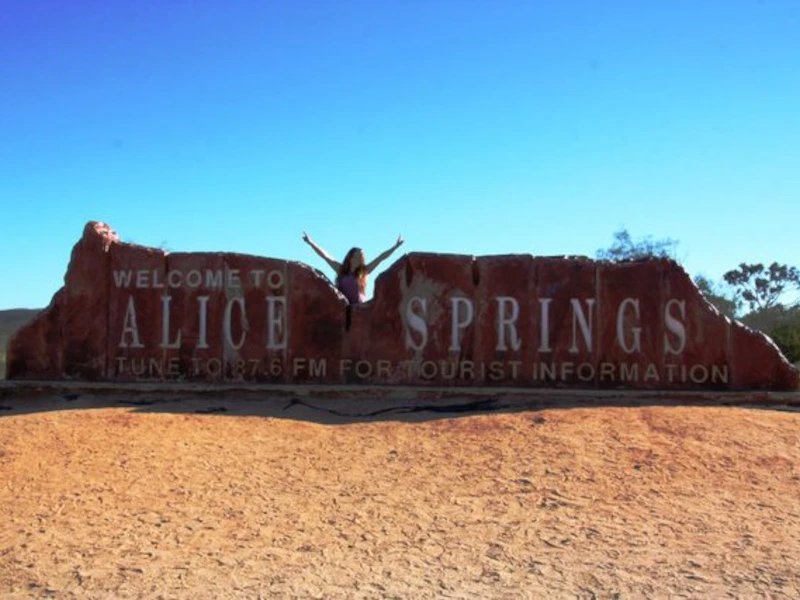 Frau mit den Armen nach oben, hinter dem Alice Springs Sign in Australien