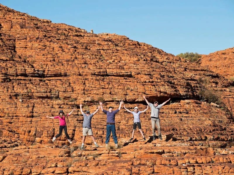 Gruppe springt vor roter Felswand im Kings Canyon, Australien
